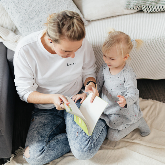 Kvinde læser højt for pige på tæppe