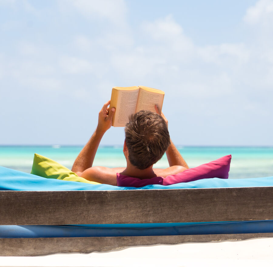 Billede af mand der læser en bog på en eksotisk strand